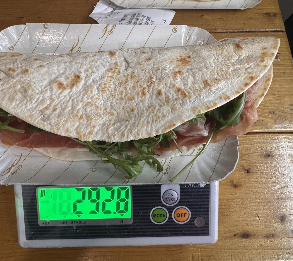 La piada Standard di Fam da Lóv con crudo e rucola in una vaschetta sulla bilancia: il display segna 292,8 grammi.